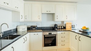 A modern kitchen with white cabinets, a granite countertop, a built-in oven, and a coffee maker. - 8 Sunday School Court (St Ives)