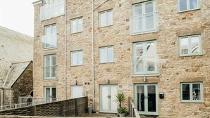 A multi-story stone building with balconies, a staircase, and a small garden area. - 8 Sunday School Court (St Ives)