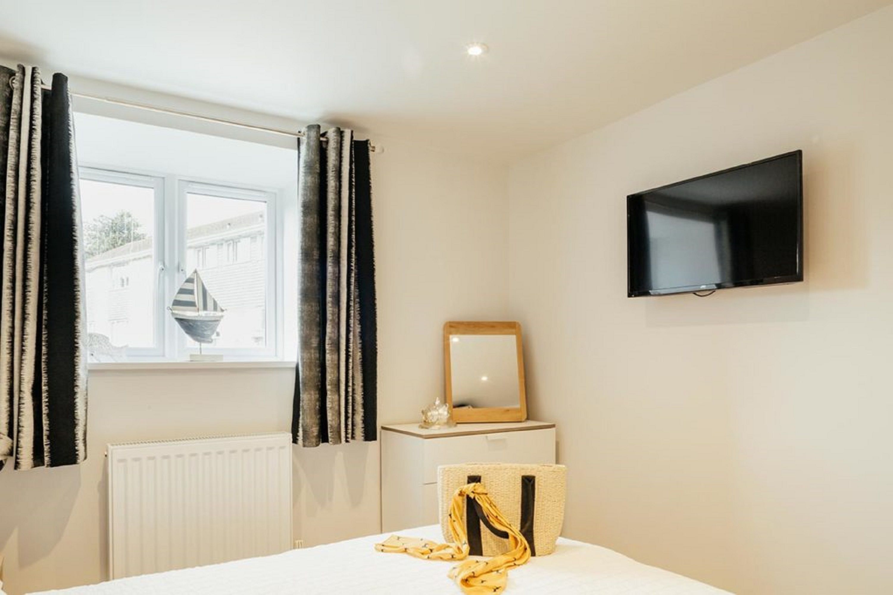 A hotel room with a bed, a TV mounted on the wall, a window with curtains, and a radiator.