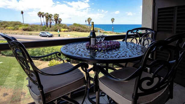 Une terrasse avec une table ronde et des chaises, une bouteille de champagne et des verres posés sur la table.