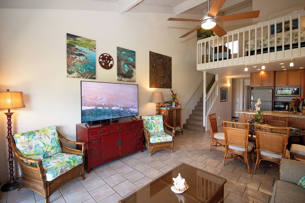 A spacious living room with a large flat-screen TV, wicker furniture, and artwork on the walls.