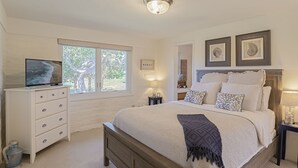 A bedroom with a bed, a dresser, a television, and a window with a view of trees. - 3786 Adobe by the Sea ~ Golf View, Walk to Beach (Pebble Beach®)