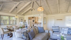 A spacious living area with a high ceiling and exposed beams, a dining table with chairs, a sofa with patterned cushions, and a kitchen area visible through an open door. - 3786 Adobe by the Sea ~ Golf View, Walk to Beach (Pebble Beach®)