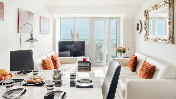 Una sala moderna con comedor, muebles blancos y un amplio ventanal con vistas a la ciudad.