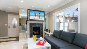 A living room with a fireplace, a flat-screen TV, a gray sofa, and a coffee table with a tray. - Multi-Level 2BR-Fast WiFI-Free Parking!-CM1 (Costa Mesa)