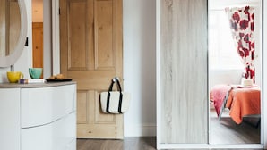 Ein Zimmer mit einem Holzschrank, einem weißen Schrank und einer Glastür zum Bett mit orangefarbener Bettdecke.