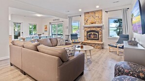 A spacious living room with a beige sofa, a stone fireplace, and a large window offering a view of the outdoors. - Group Getaway w/ Dock! Lakefront Escape in Stover (Stover)