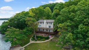 A two-story house with a deck, surrounded by dense trees and a lake. - Group Getaway w/ Dock! Lakefront Escape in Stover (Stover)