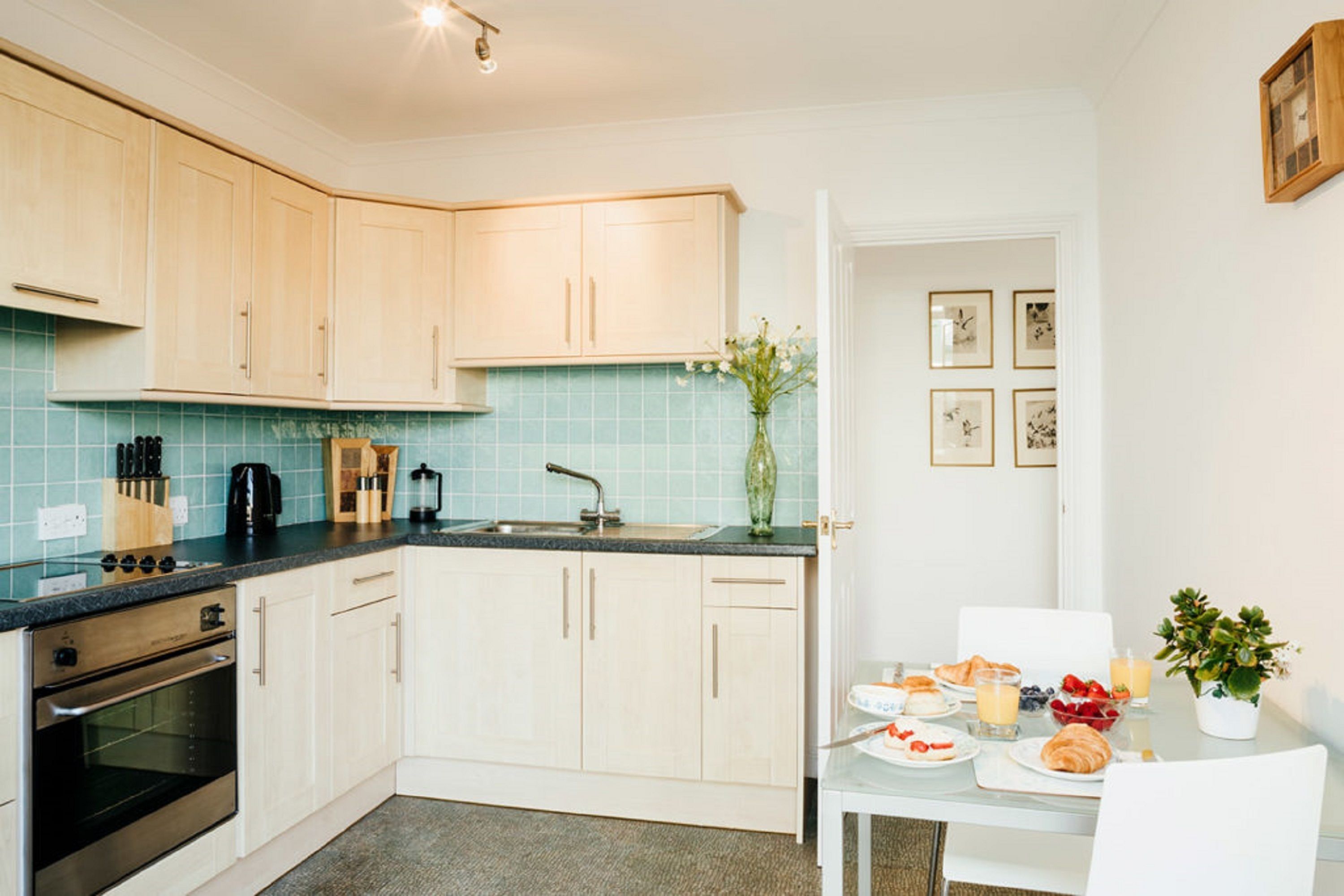 A modern kitchen with light wood cabinets, a black oven, and a blue tiled backsplash.