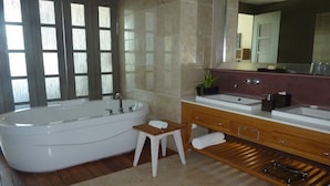 A bathroom with a freestanding bathtub, a vanity with a mirror, and a small wooden stool. - The Lux Luxxe Spa Tower (Nuevo Vallarta)