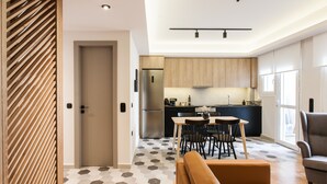 A modern kitchen with wooden cabinets, a stainless steel refrigerator, and a dining area with a table and chairs. - UPSTREET Modern Minimalist 3BD Apt-Hilton (Athens)