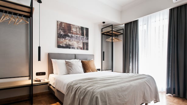 A modern bedroom with a bed, a bench, a hanging light, and a large window with curtains. - UPSTREET Modern Minimalist 3BD Apt-Hilton (Athens)