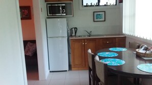 Une cuisine avec un réfrigérateur blanc, un four à micro-ondes, des armoires en bois, un évier et une table à manger avec des sets de table bleus.