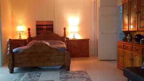 Une chambre à coucher avec un lit en bois, deux tables de chevet avec des lampes, une armoire et une porte donnant sur une autre pièce.