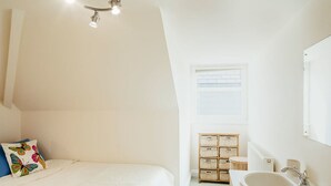 Une chambre à coucher comprenant un lit, une table de chevet, une commode, une fenêtre avec des stores et une petite commode en bois.