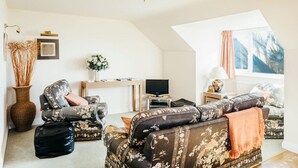 Un salon comprenant un canapé, un téléviseur, un vase avec des plantes séchées et une fenêtre avec des rideaux.