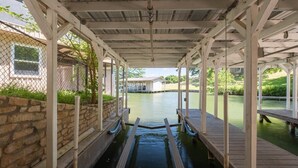 A covered outdoor area with a wooden deck, stone walls, and a view of a house across a body of water. - Paradise Cove- Lakefront on a Cove w/Guest Cottage (Kingsland)