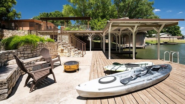 A wooden deck with a kayak, chairs, and a covered area overlooking a body of water. - Paradise Cove- Lakefront on a Cove w/Guest Cottage (Kingsland)