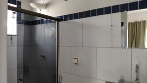 Et badeværelse med glasbrusekabine, bøjle til håndklæder, spejl og et håndklæde hængende på væggen.