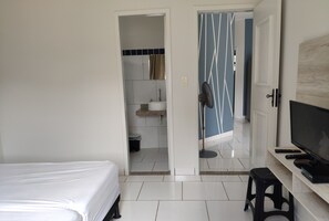 Ein Hotelzimmer mit einem Bett, einem Fernseher, einem Hocker und einem durch eine offene Tür einsehbaren Badezimmer.