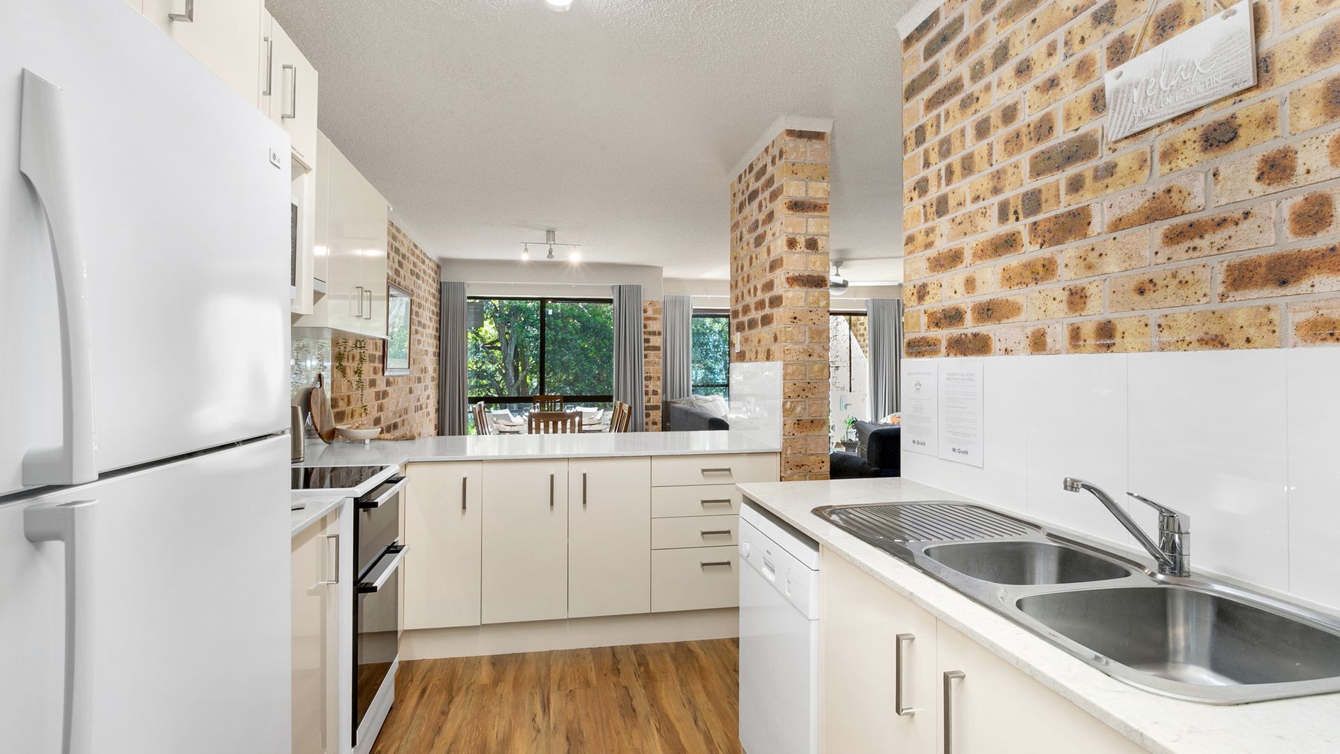 A modern kitchen with white cabinetry, a brick accent wall, and a large window providing a view of the outdoors.