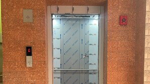 An elevator with a digital display, emergency contact sign, and directional arrows on the walls. - Nimmu House (Kumta)