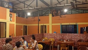 A restaurant with brick walls, yellow and orange decor, and multiple tables and chairs. - Nimmu House (Kumta)