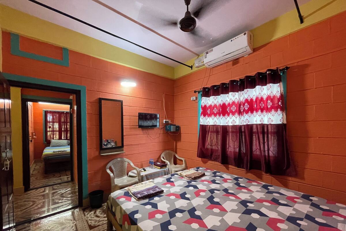 A room with a bed, two chairs, a television, and a ceiling fan.