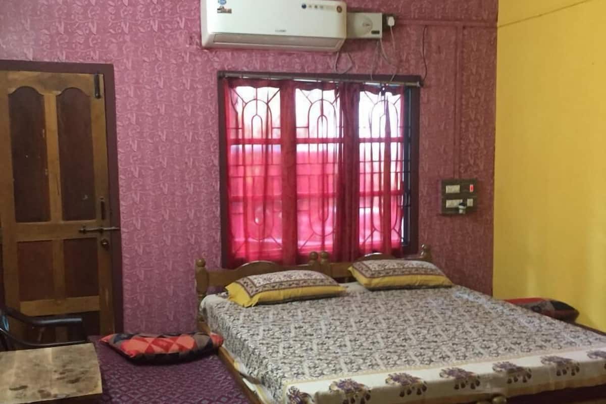A bedroom with a bed, a ceiling fan, an air conditioning unit, a window with curtains, and a door.