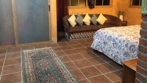 Una habitación acogedora con una cama, un sofá con cojines, un tapete estampado y una ventana con cortinas.