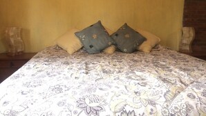 Una cama con un edredón estampado con motivos florales y dos almohadones decorativos.