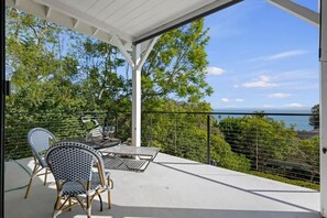 Un patio al aire libre con una mesa y sillas, rodeado por una barandilla blanca y vistas panorámicas.