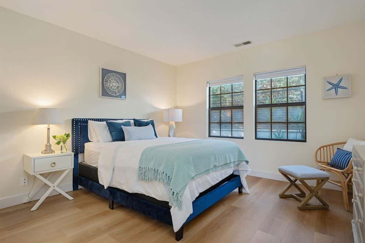 A bedroom with a bed, bedside tables, a chair, and two windows.