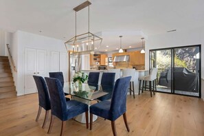 A modern kitchen with a central island, a dining area with a glass table and blue chairs, and a staircase leading to another level. - Summerland Sea View (Summerland)