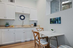 A compact kitchen with white cabinets, a stainless steel sink, and a dining area with a white table and wooden chairs. - Summerland Sea View (Summerland)
