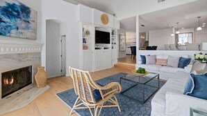 En moderne stue med pejs, en hvid sofa, en fletstol og et fladskærms-tv på et hvidt skab.