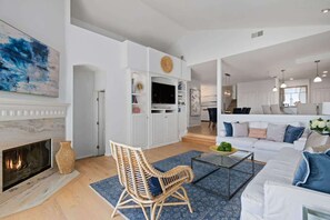 A modern living room with a fireplace, a white sofa set, a wicker chair, and a flat-screen TV on a white cabinet. - Summerland Sea View (Summerland)