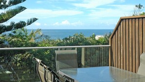 A balcony with a view of the ocean, a table, and chairs. - Angourie Blue 8 Now Pets considered (Angourie)