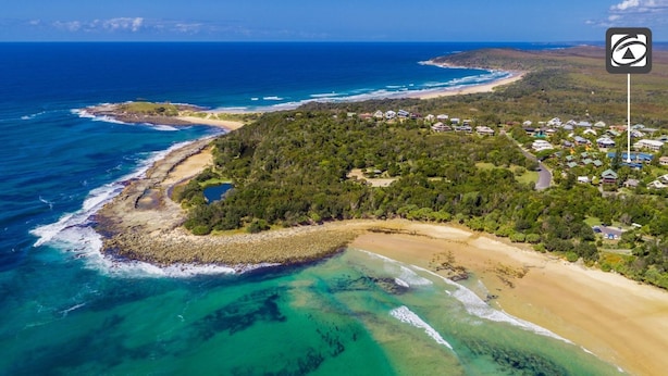 An aerial view of a coastal area with a beach, rocky shoreline, and a cluster of houses surrounded by greenery. - Angourie Blue 8 Now Pets considered (Angourie)