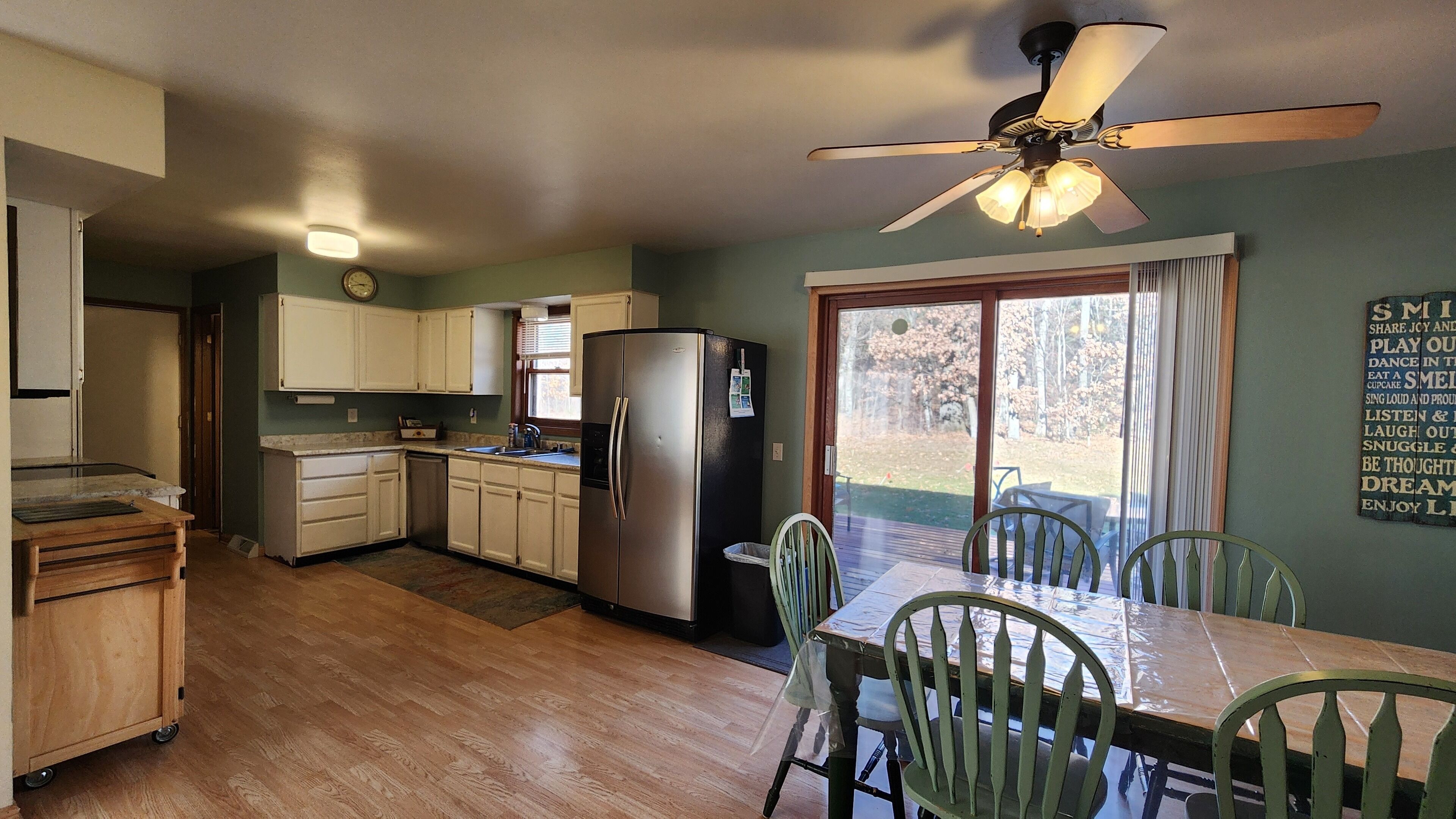 A compact kitchen with a refrigerator, sink, and wooden cabinets. There is a dining area with a table and chairs, and a ceiling fan above.