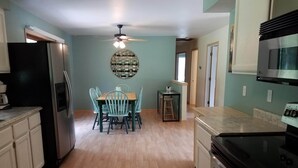 A kitchen with a dining area, wooden flooring, a ceiling fan, and a refrigerator.