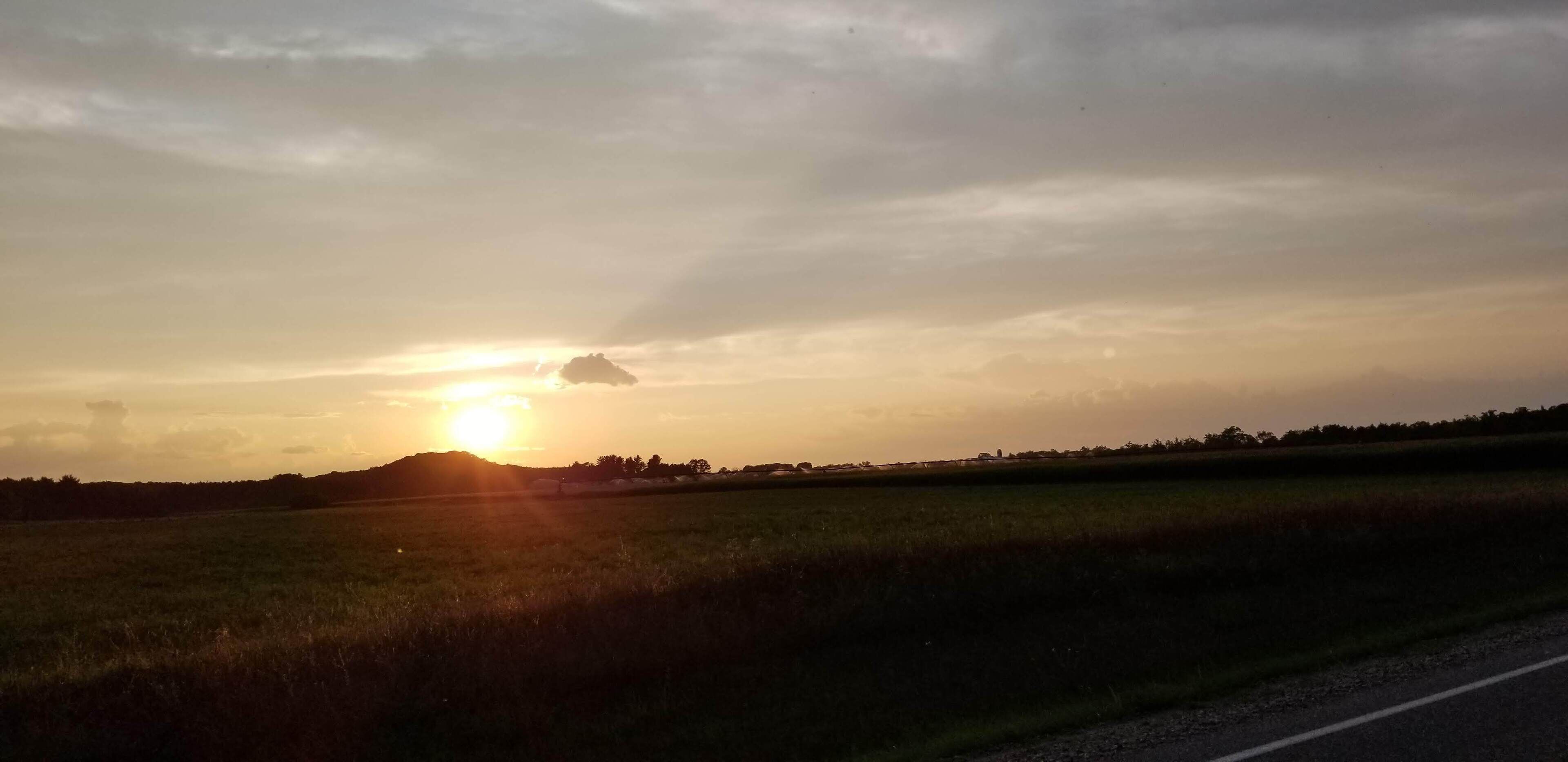 A sunset over a flat landscape with a road in the foreground.