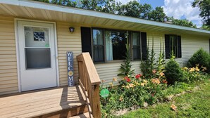 A single-story house with a front porch, a welcome sign, and a front door with a window.
