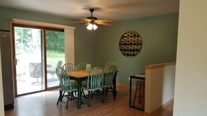 A dining area with a wooden table and four chairs, a ceiling fan, and a view through a glass door to an outdoor patio.