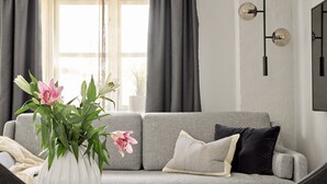 Un salon avec un canapé gris, un vase blanc orné de fleurs et une table sur laquelle repose un magazine.