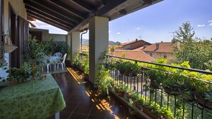 Ein Balkon mit Tisch und Stühlen, Blumentöpfen und Blick auf Gebäude und Hügel.