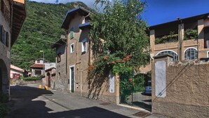 Eine enge Straße mit traditionellen Gebäuden, einer Steinmauer und einem Baum mit roten Blüten.