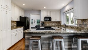 A modern kitchen with white cabinets, granite countertops, a black refrigerator, a microwave, and a large island with bar stools.