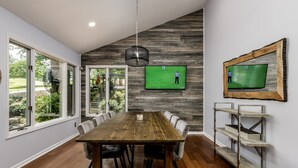 A dining area with a wooden table, chairs, a TV mounted on the wall, and a fan.