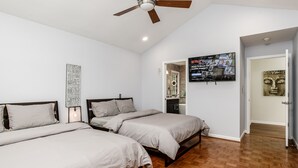 A bedroom with two beds, a ceiling fan, a wall-mounted TV, and a wooden floor.